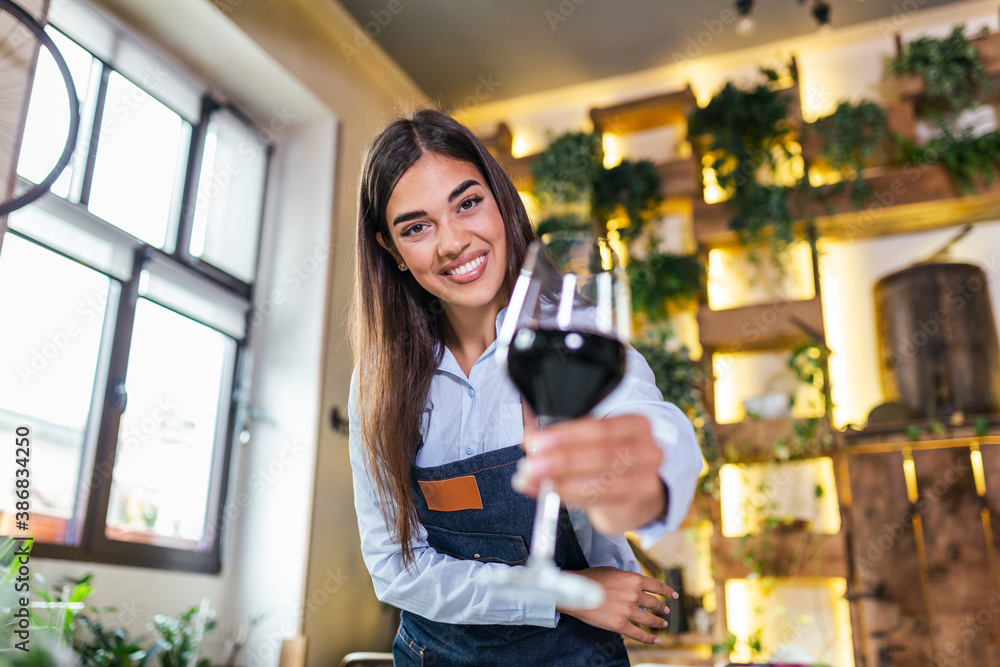 Young beautiful waitress wearing apron holding a glass of red wine in one hand serving a customer in a rustic restaurant. Sommelier recommended wine in restaurant. Young beautiful waitress wearing apron holding a glass of red wine in one hand serving a customer in a rustic restaurant. Sommelier recommended wine in restaurant.