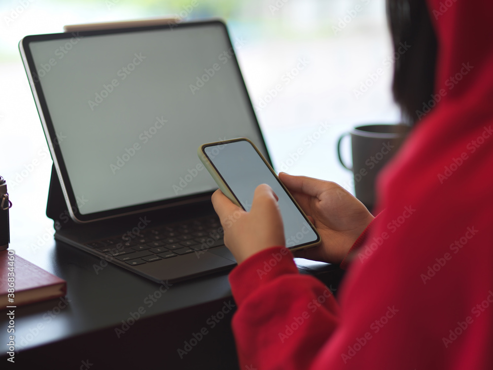 Fototapeta premium Side view of female in red sweater using mock up smartphone and tablet