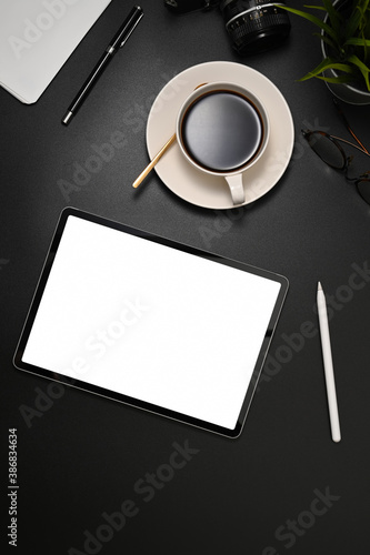 Workspace with tablet, coffee cup and supplies on black table