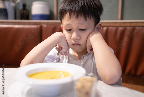 Depressed asian kid boy with anorexia,don't have appetite,child kindergarten bored with food or boredom,refusing to eat vegetable soup,unpalatable,tired of food,nutrition and eating disorder concept