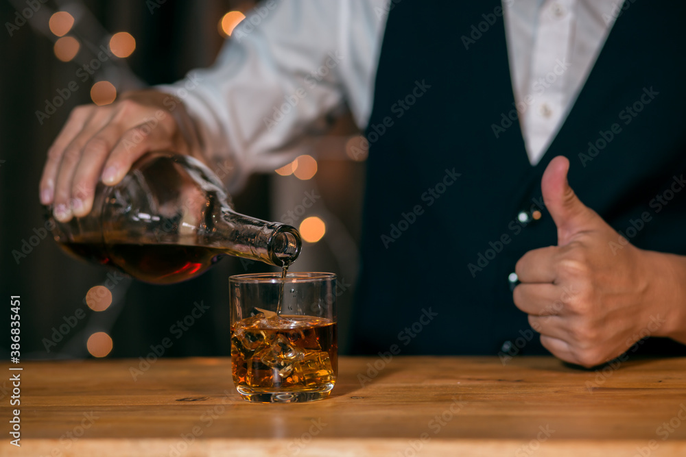 Waitress man standing pours whiskey into a glass 