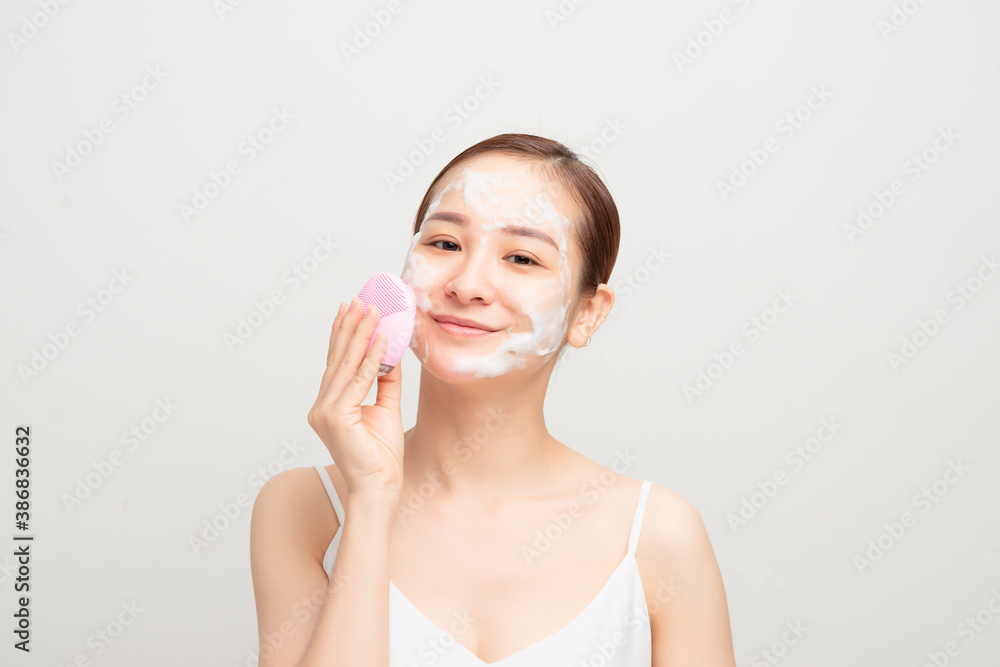 Young woman using facial cleansing brush on white background, closeup. Washing accessory Young woman using facial cleansing brush on white background, closeup. Washing accessory
