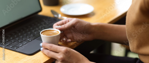 Side view of female hands holding coffee cup while sitting at workplace