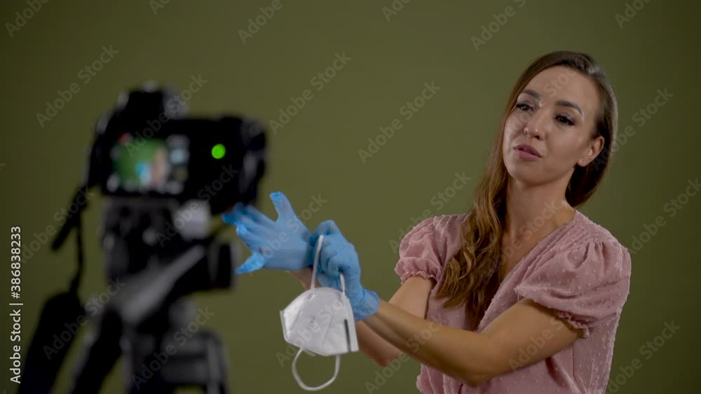 Young woman recording a video tutorial during COVID-19 pandemic, explaining how to put on medical gloves. Green background. Young woman recording a video tutorial during COVID-19 pandemic, explaining how to put on medical gloves. Green background.