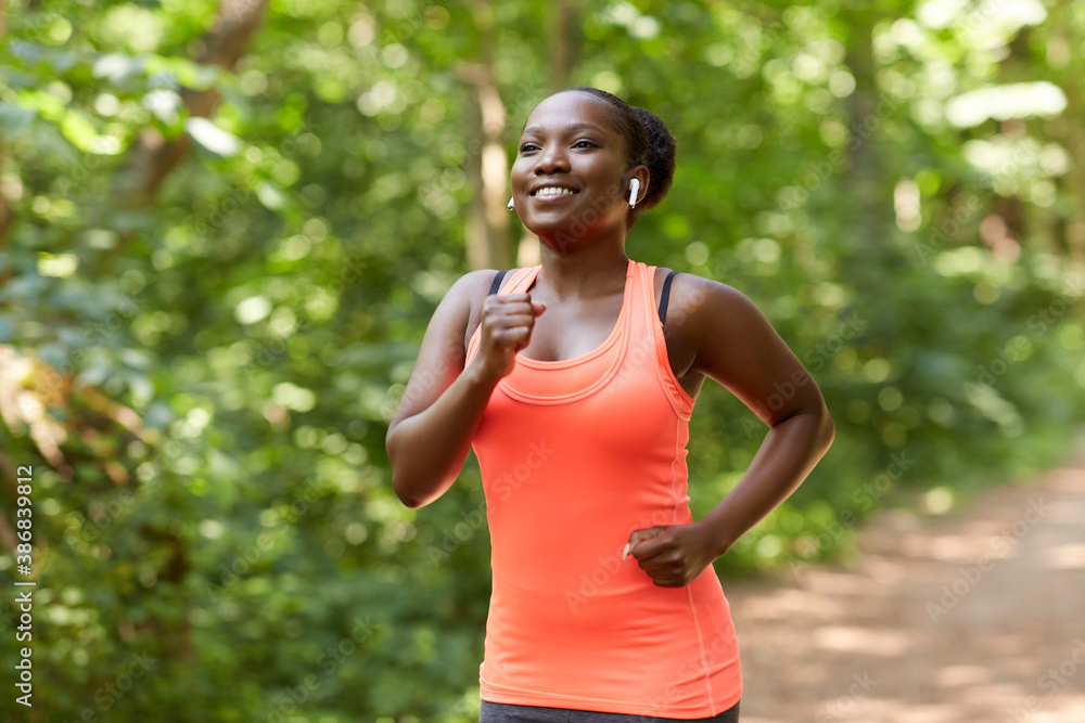 fitness, sport and healthy lifestyle concept - happy smiling young african american woman with earphones running in park fitness, sport and healthy lifestyle concept - happy smiling young african american woman with earphones running in park
