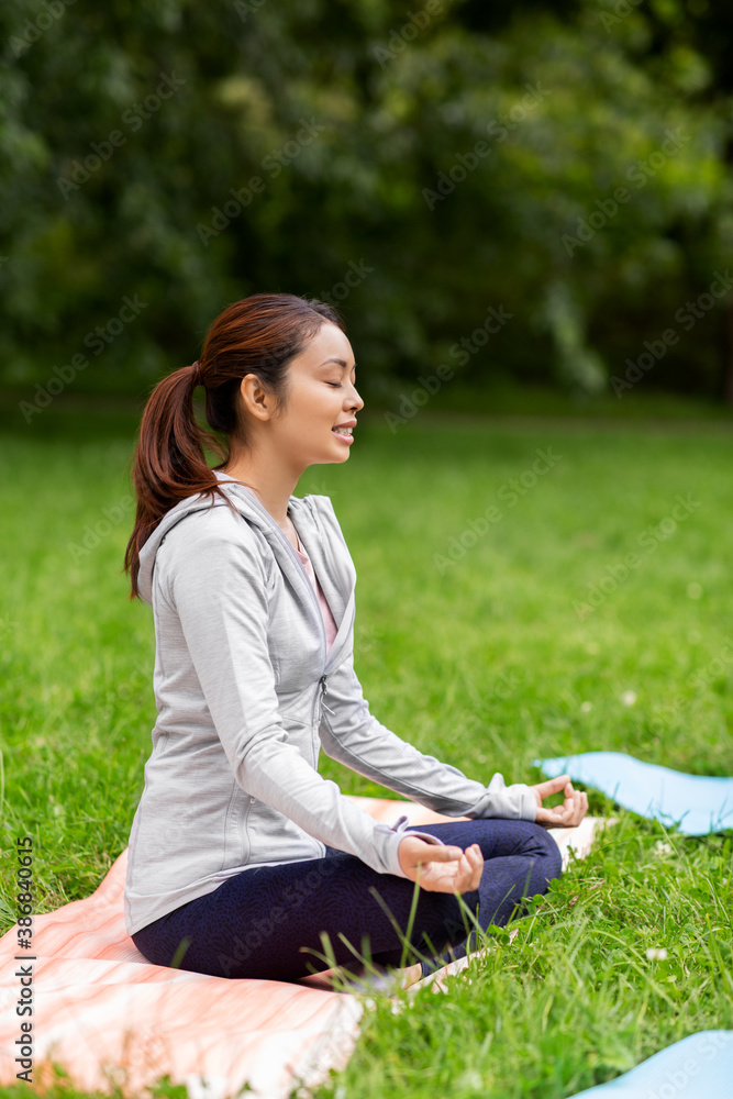 fitness, sport, yoga and healthy lifestyle concept - young asian woman meditating in lotus pose at summer park