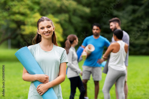 fitness, sport and healthy lifestyle concept - happy smiling young woman with mat over group of people meeting for yoga class at summer park