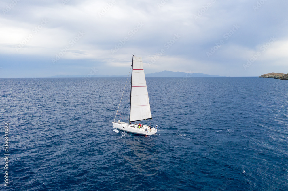 Sailing boat with white sails, cloudy sky and rippled sea background