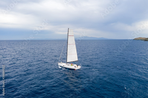 Sailing boat with white sails, cloudy sky and rippled sea background © Rawf8