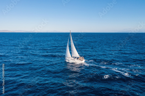 Sailing boat with white sails, cloudy sky and rippled sea background