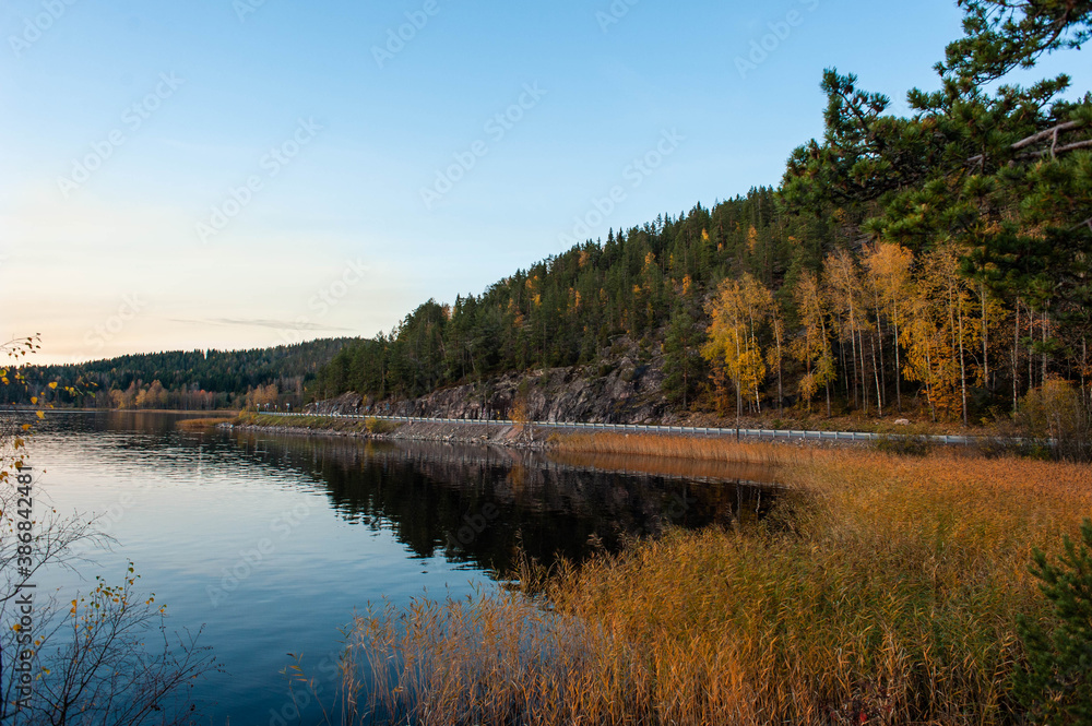 It's a beautiful sunset scenery. A lake with rocky shores and autumn forest on hilly terrain.