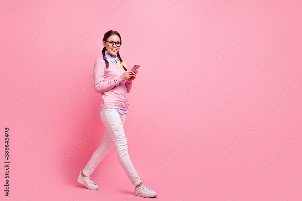 Full length body size view of her she attractive lovely pretty cheerful cheery girl geek strolling using digital device 5g app posting comment feedback isolated over pink pastel color background Full length body size view of her she attractive lovely pretty cheerful cheery girl geek strolling using digital device 5g app posting comment feedback isolated over pink pastel color background