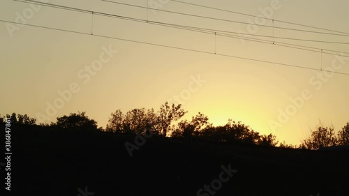 Passenger train with compartments of corridor coaches rides on the railway at sunset in silhouette. Railroad carriage wagons going in daytime. Travel and tourism. photo