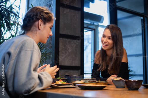 Two happy girls eating and having fun while communicating in a cafe.