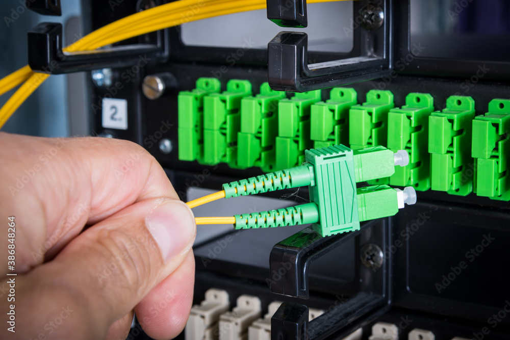 Hand of computer engineer connecting fiber optic cable in server