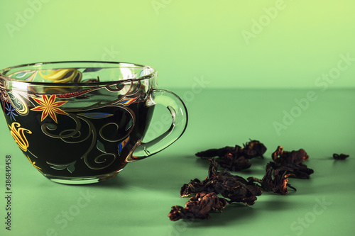 Beautiful glass cup with karkade tea on a green background with copy space.