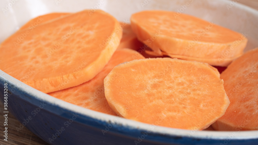 Sliced sweet potato on top of each other in a ceramic casserole. The bright orange herb staple is a healthy replacement for potato or french fries. Concept for displaying food in fall colors. Sliced sweet potato on top of each other in a ceramic casserole. The bright orange herb staple is a healthy replacement for potato or french fries. Concept for displaying food in fall colors.