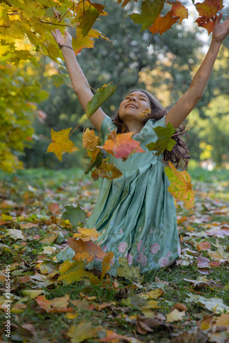 Portrait of a girl in a green dress playing in a Park with colorful maple leaves  in a state of absolute happiness