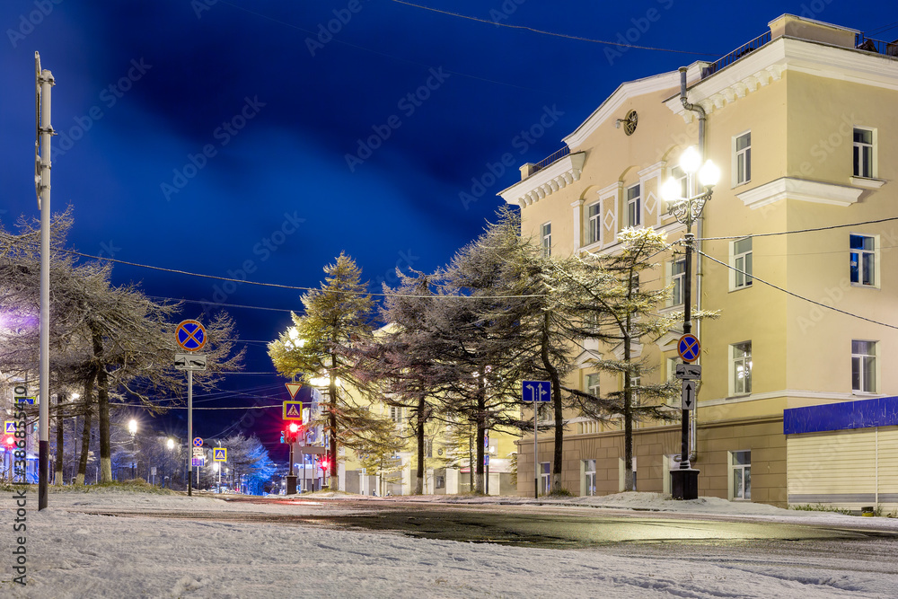 Night city landscape. Snow-covered empty street in the historical center of Magadan. Magadan region, Siberia, Far East of Russia. There is no one on the street.