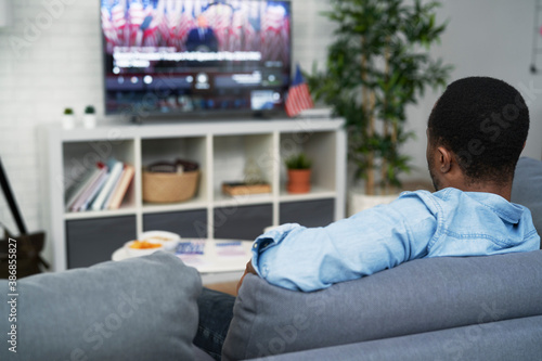 Rear view of black man watching USA election on TV