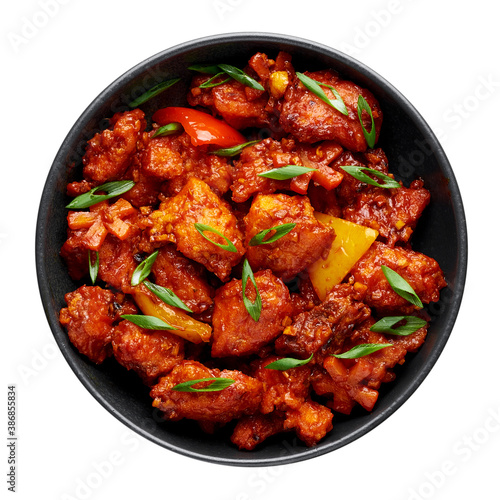 Fish Manchurian dry looks like Schezwan Fish in black bowl isolated on white background. Fish Manchurian - is indo chinese cuisine dish with deep fried salmon, bell peppers, sauce and onion. Top view.
