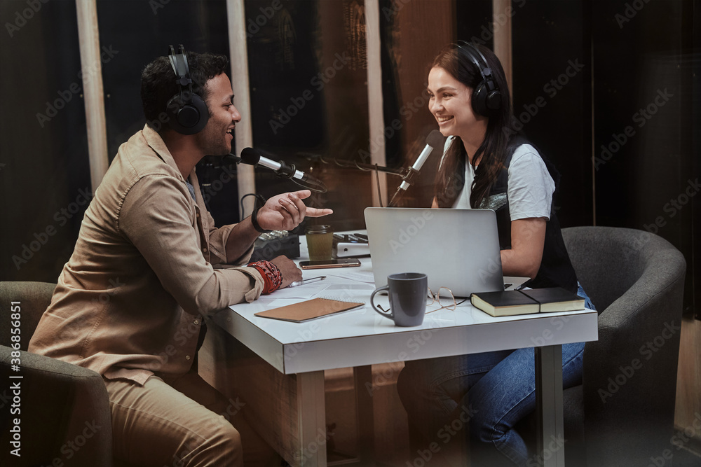 Portait of two happy radio hosts, young man and woman smiling while discussing various topics, moderating a live show in studio
