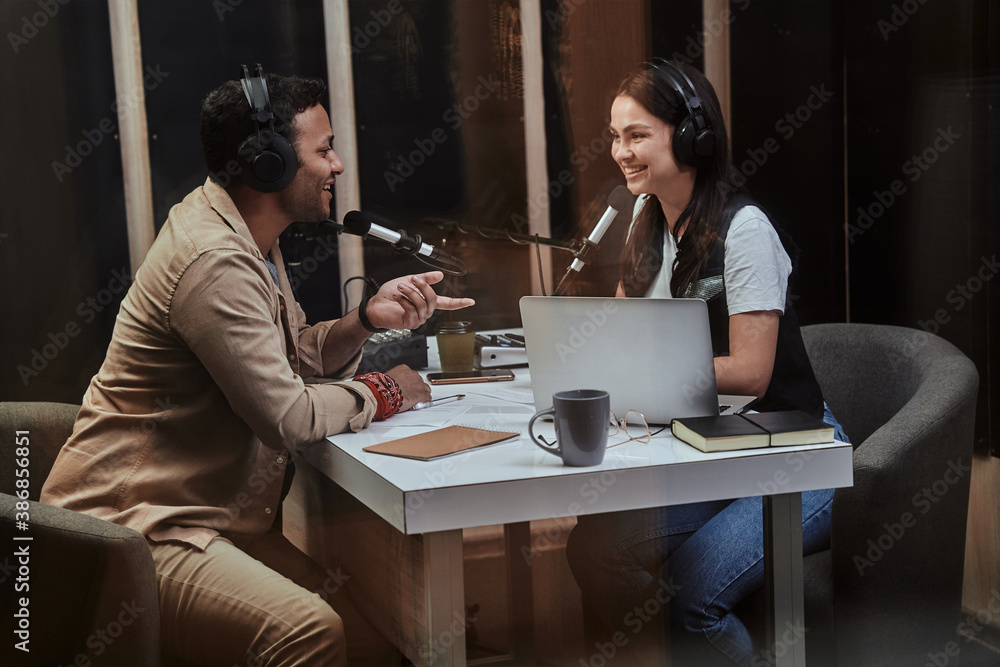Portait of two happy radio hosts, young man and woman smiling while discussing various topics, moderating a live show in studio Portait of two happy radio hosts, young man and woman smiling while discussing various topics, moderating a live show in studio