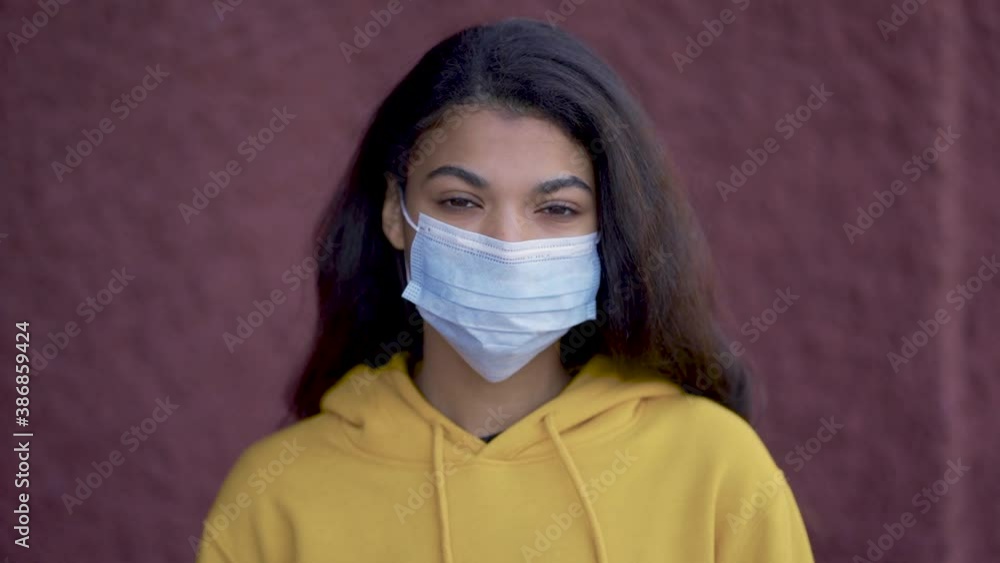 New normal concept. Portrait of young pretty black woman pointing at her medical face mask outdoors. Protection against the COVID-19 pandemic. New normal concept. Portrait of young pretty black woman pointing at her medical face mask outdoors. Protection against the COVID-19 pandemic.