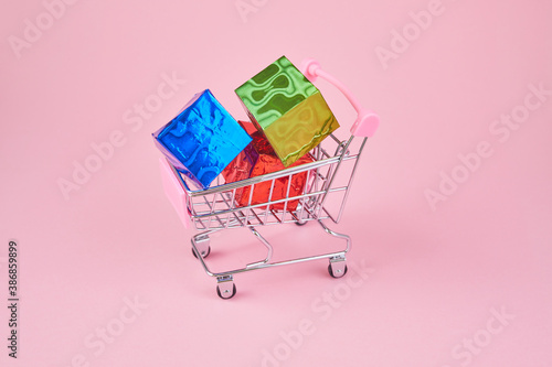 Gift shopping. Shopping cart is full of colourful gift boxes on pink background.
