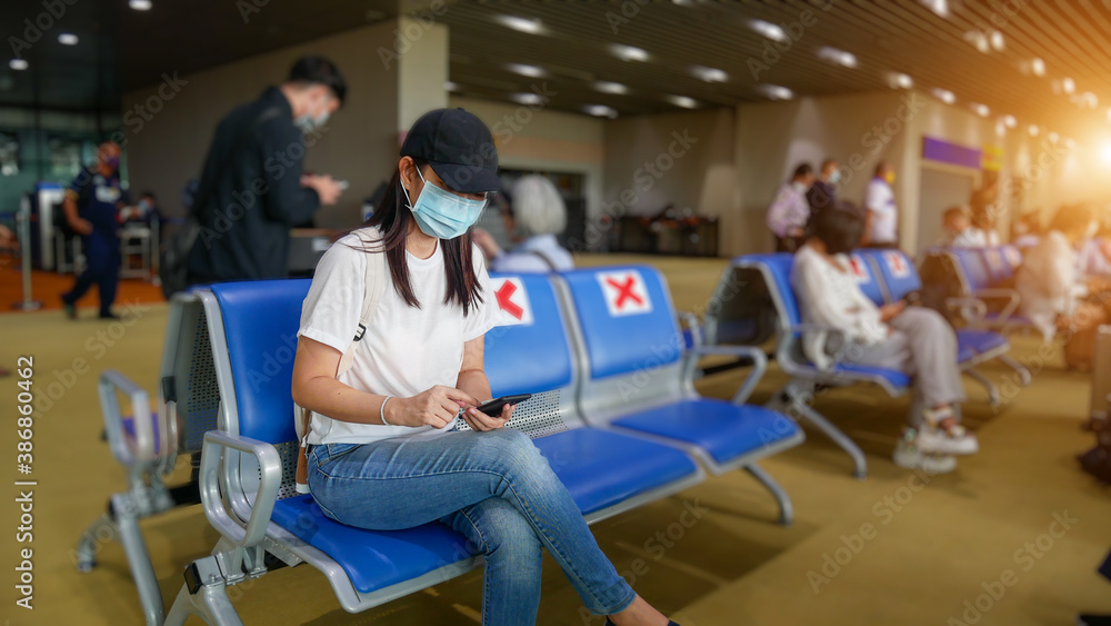 Asian tourist with mobile phone ,wearing hygienic mask, sit on chair with social distancing to prevent pandemic during travel at airport terminal. new normal after coronavirus, covid-19 virus epidemic - obrazy, fototapety, plakaty 