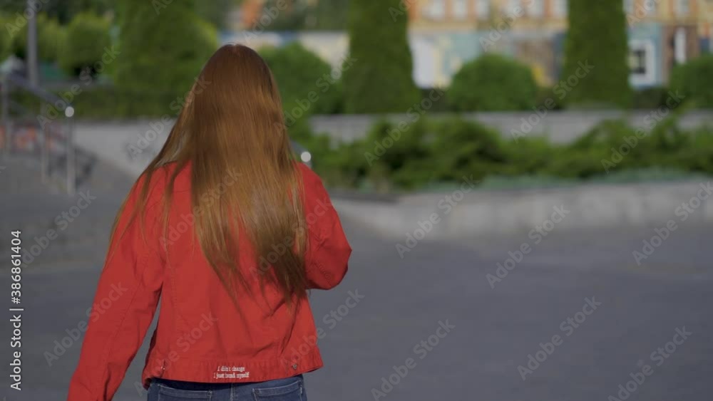 Young pretty red-haired excited woman smiling and walking outdoors. Happy caucasian female. View from behind. Young pretty red-haired excited woman smiling and walking outdoors. Happy caucasian female. View from behind.
