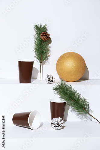 Minimal golden ball  with winter brunch and cup decor on white trendy space. Fashion still life art. Merry Christmas / Happy New Year holidays celebration concept.