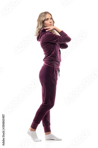 Side view of confident young pretty woman getting dressed in leisurewear tracksuit looks at camera. Full body isolated on white background.