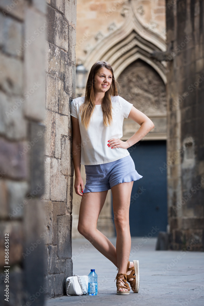 Happy young woman strolling around city standing near old stone wall