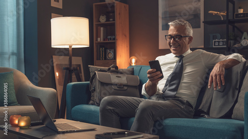 Businessman relaxing on the sofa at home and connecting with his phone