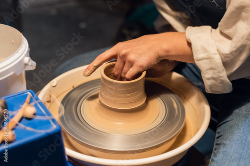 master class on sculpting a pot in an art workshop. the girl behind the potter's wheel makes a blank with her hands