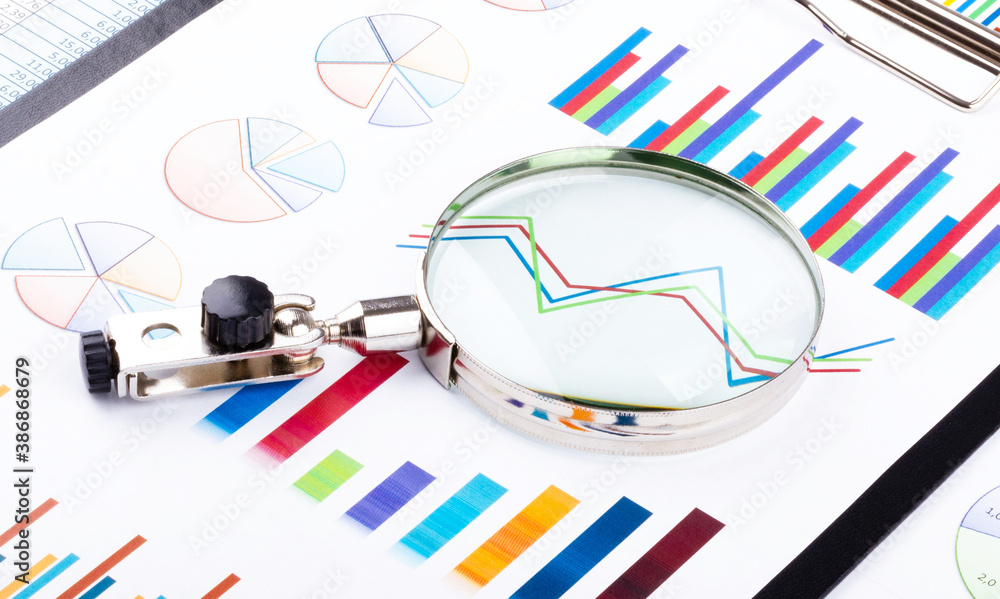 Magnifying glass lying on business charts and graphs. Business planning,accounting,analysis,financial planning and data Analysis concept. Magnifying glass lying on business charts and graphs. Business planning,accounting,analysis,financial planning and data Analysis concept.