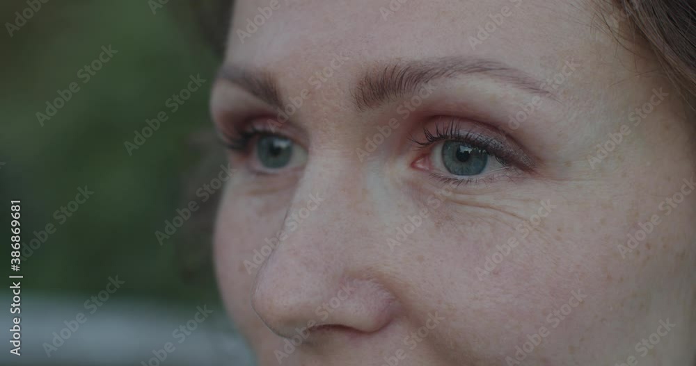 Extra close up portrait of woman smiling outdoors on defocused green background. Grey female eyes looking with joy sideways shallow dof slow motion. Beauty skin care facial cosmetics concept Extra close up portrait of woman smiling outdoors on defocused green background. Grey female eyes looking with joy sideways shallow dof slow motion. Beauty skin care facial cosmetics concept