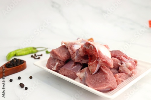 Fresh raw goat meat or mutton or lamb pieces. Preparation for Indian mutton curry. Spice at the background such as cinnamon sticks, red chili powder, black pepper & coriander. Copy space.