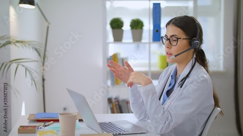 Young Female Doctor Wears White Coat, Video Calling Distant Patient on Laptop. Doctor Talking to Client in Home Office Visit Computer app. Telemedicine, Remote Healthcare Services Concept Video Call
