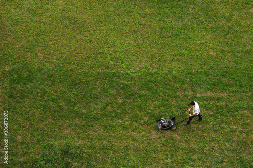 Man mowing the lawn.A lawn mower is cutting green grass, the gardener with a lawn mower is working in the backyard, a side view.