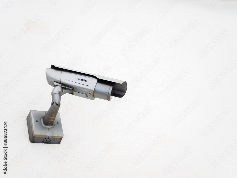 Silver CCTV camera angled to the side on a white wall Silver CCTV camera angled to the side on a white wall