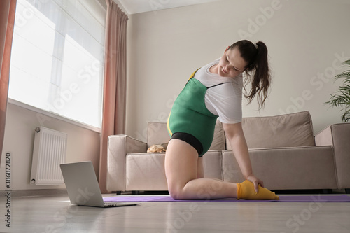 Female plus-size model sports at home online in sportswear. A pet, a small dog, is sleeping on the sofa. Playing sports at home during the pandemic.