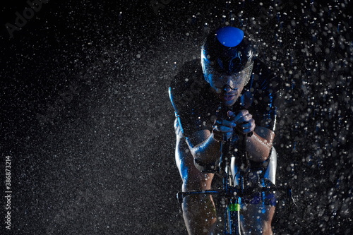 Фотография triathlon athlete riding bike fast on rainy night