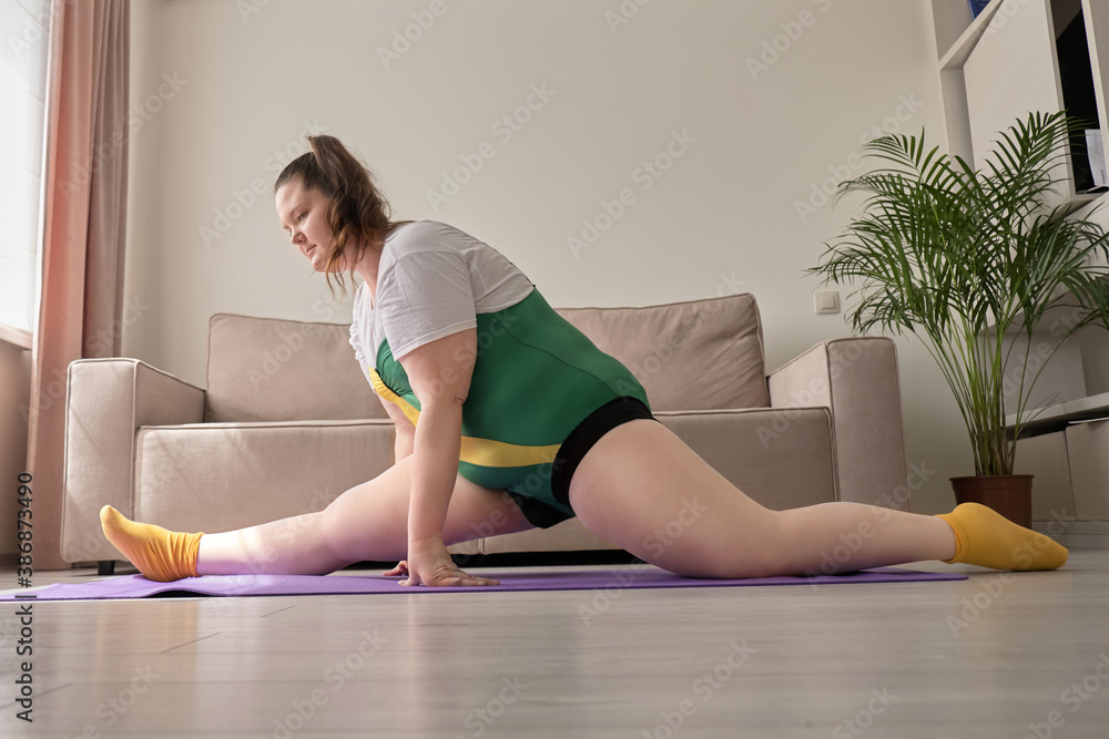 Young woman, plus size, sit down on the splits next to a laptop. Sports during the pandemic. Young woman, plus size, sit down on the splits next to a laptop. Sports during the pandemic.