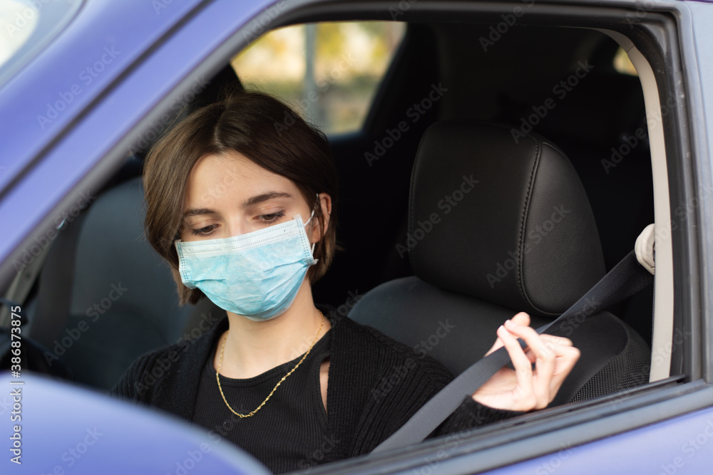 Young woman with surgical mask putting on seat belt in car Young woman with surgical mask putting on seat belt in car