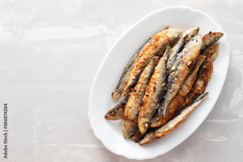 fried small sardines on white dish on ceramic background