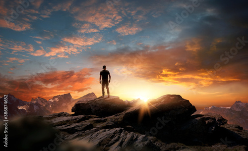 A man standing at the top of a mountain as the sun begins to set. Goals, hopes and aspirations concept. Photo compostion.