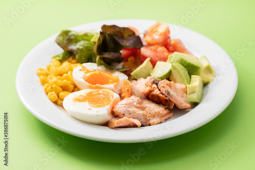 salad salmon with vegetables and boiled egg on white plate on green background