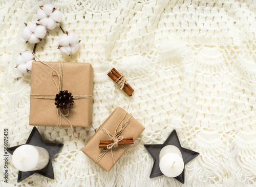 Winter composition with gifts, pine cones, cinnamon, a cotton branch on a light knitted blanket. Flat lay, top view, copy space. Warm cozy Christmas